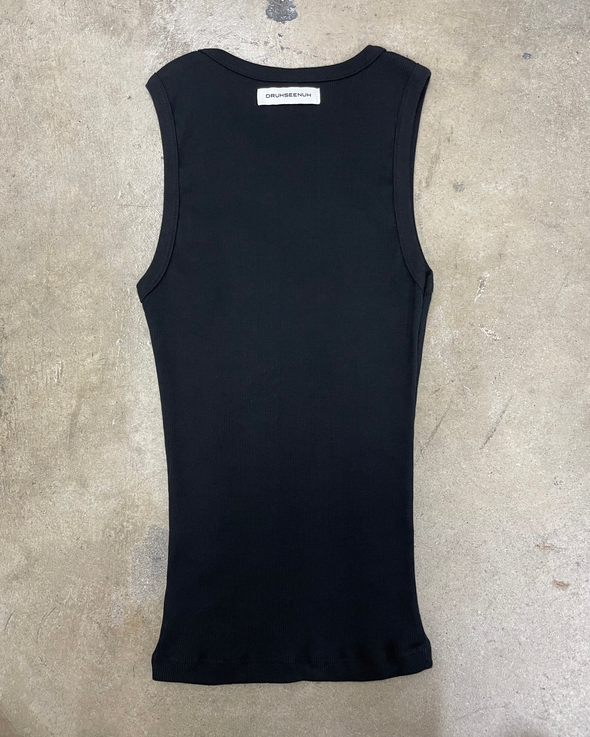 Black tank top with a brand label on a gray concrete surface
