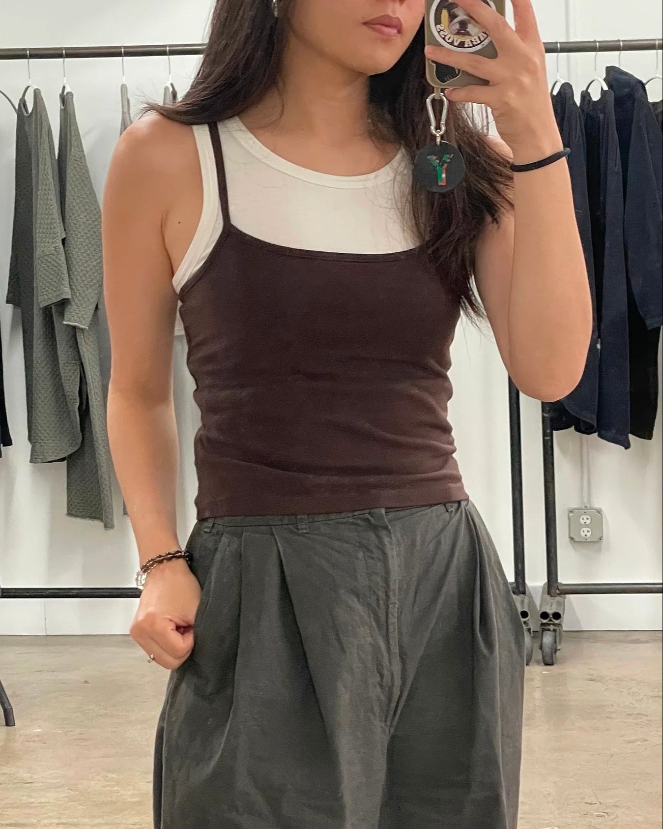 Person taking a mirror selfie wearing a brown tank top and gray pants in a clothing store.
